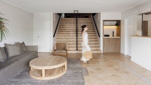 A modern living room with a sofa, a round wooden coffee table, and a staircase leading to a kitchen area. - The Lord Byron (Byron Bay)