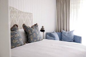 Una cama bien tendida con almohadas estampadas, una lámpara de noche y un cabecero tapizado en azul.