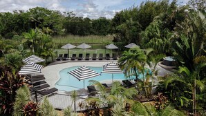 A pool area with lounge chairs and striped umbrellas, surrounded by tropical vegetation. - The Lord Byron (Byron Bay)