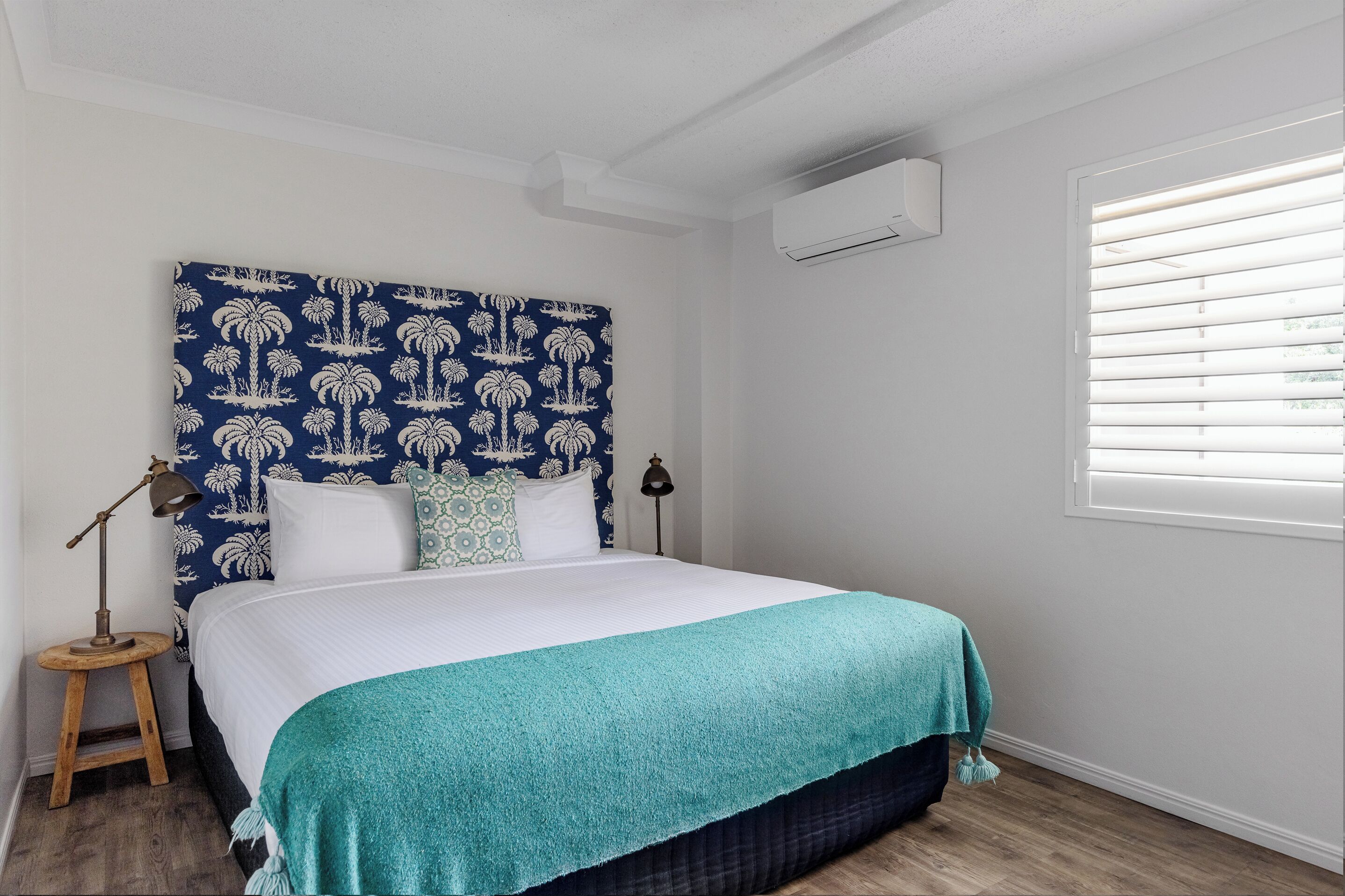 A neatly made bed with a teal blanket, a patterned headboard, and a nightstand with a lamp.