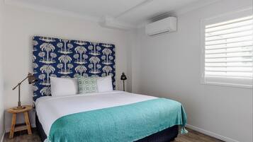 A neatly made bed with a teal blanket, a patterned headboard, and a nightstand with a lamp.