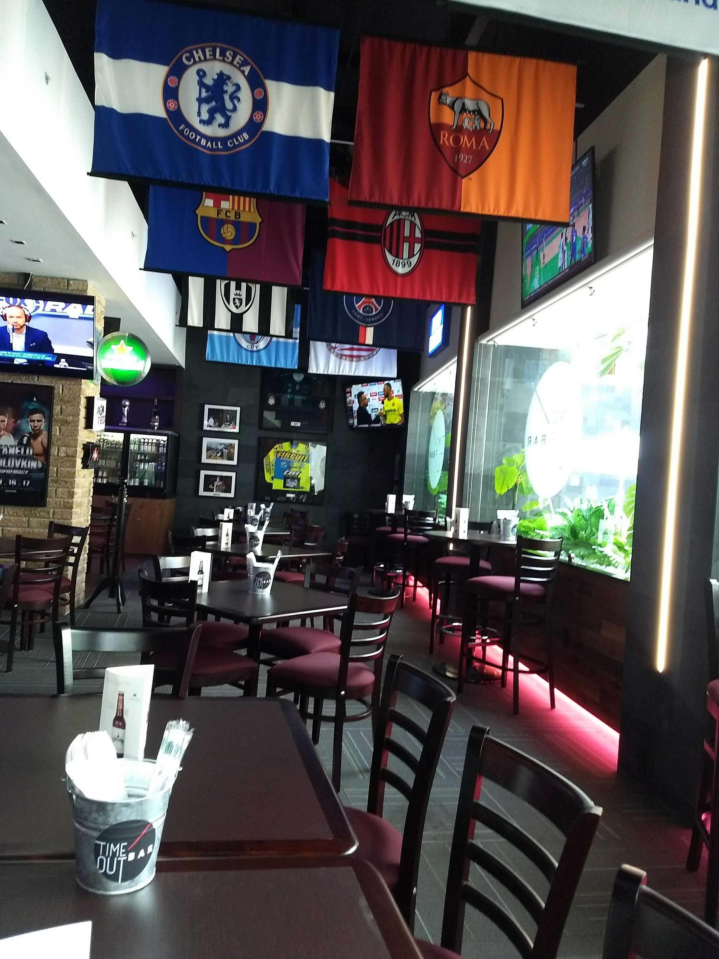 A restaurant interior with multiple tables and chairs, flags hanging from the ceiling, and a large window with a view.