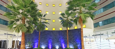 An indoor swimming pool with palm trees and a blue-lit wall.