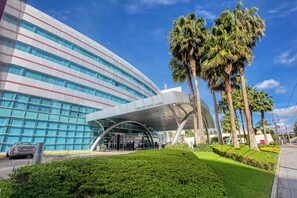 A modern building with a curved facade, a covered entrance, and palm trees in the foreground. - Crowne Plaza Leon by IHG (León)