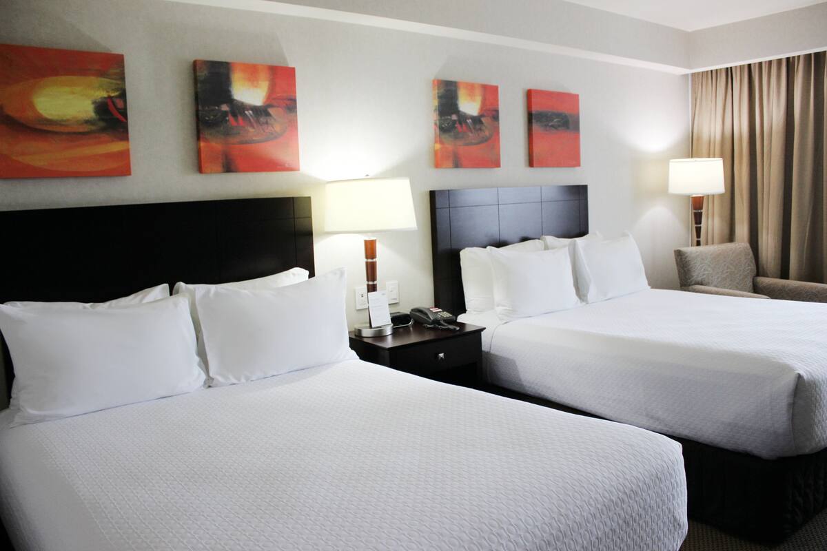A hotel room with two beds, a nightstand, a lamp, and abstract art on the wall.