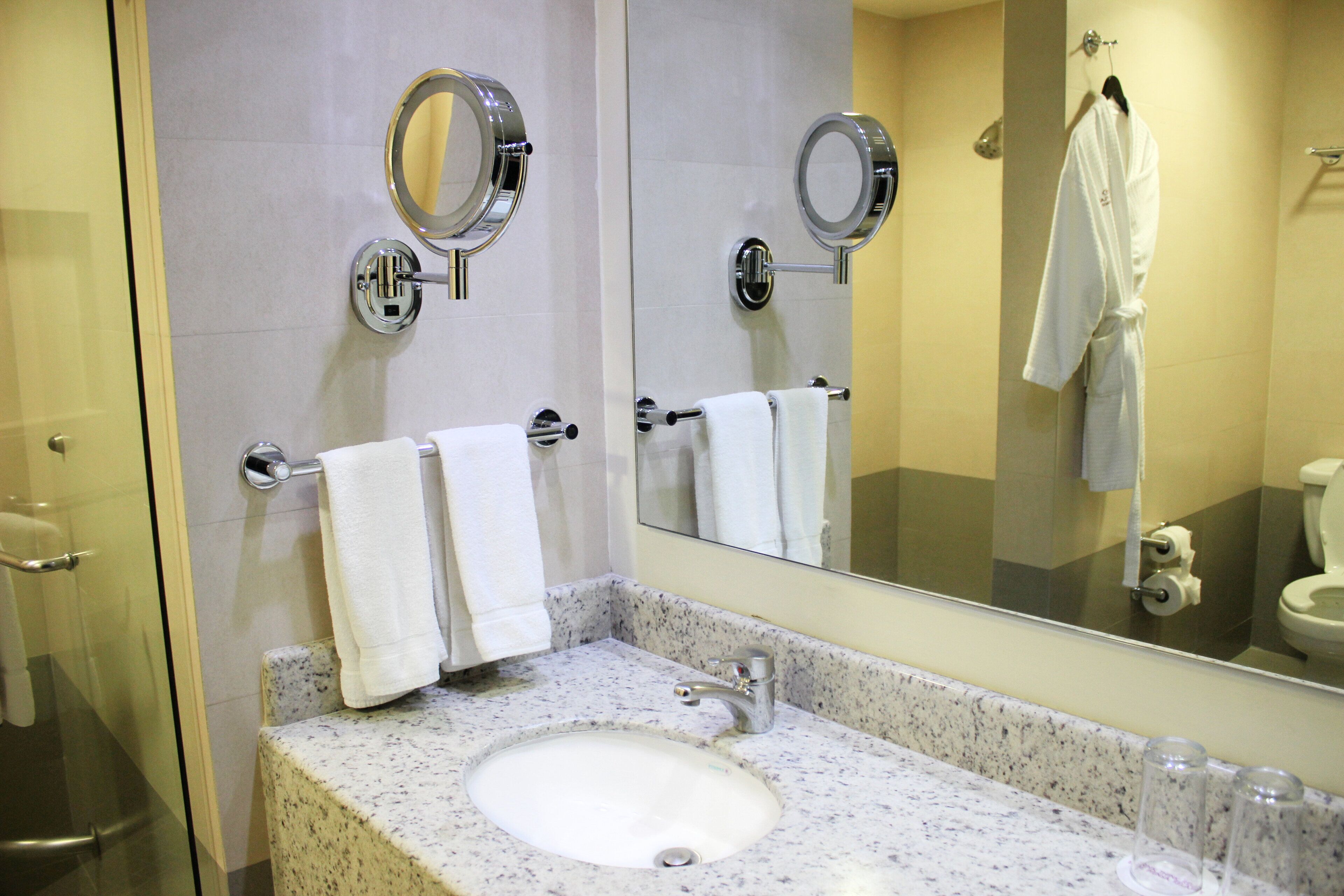 A bathroom with a sink, two mirrors, and a hanging robe.