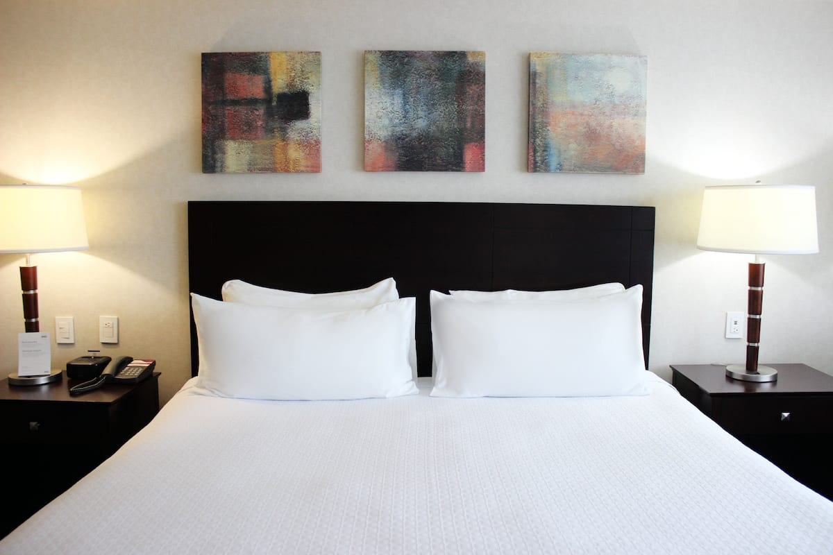 A hotel room with a large bed, two bedside tables, a black headboard, and three abstract paintings on the wall.