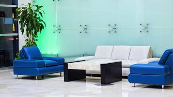 Un hall con un sofá blanco, dos sillones azules, una mesa de centro negra y una planta verde.