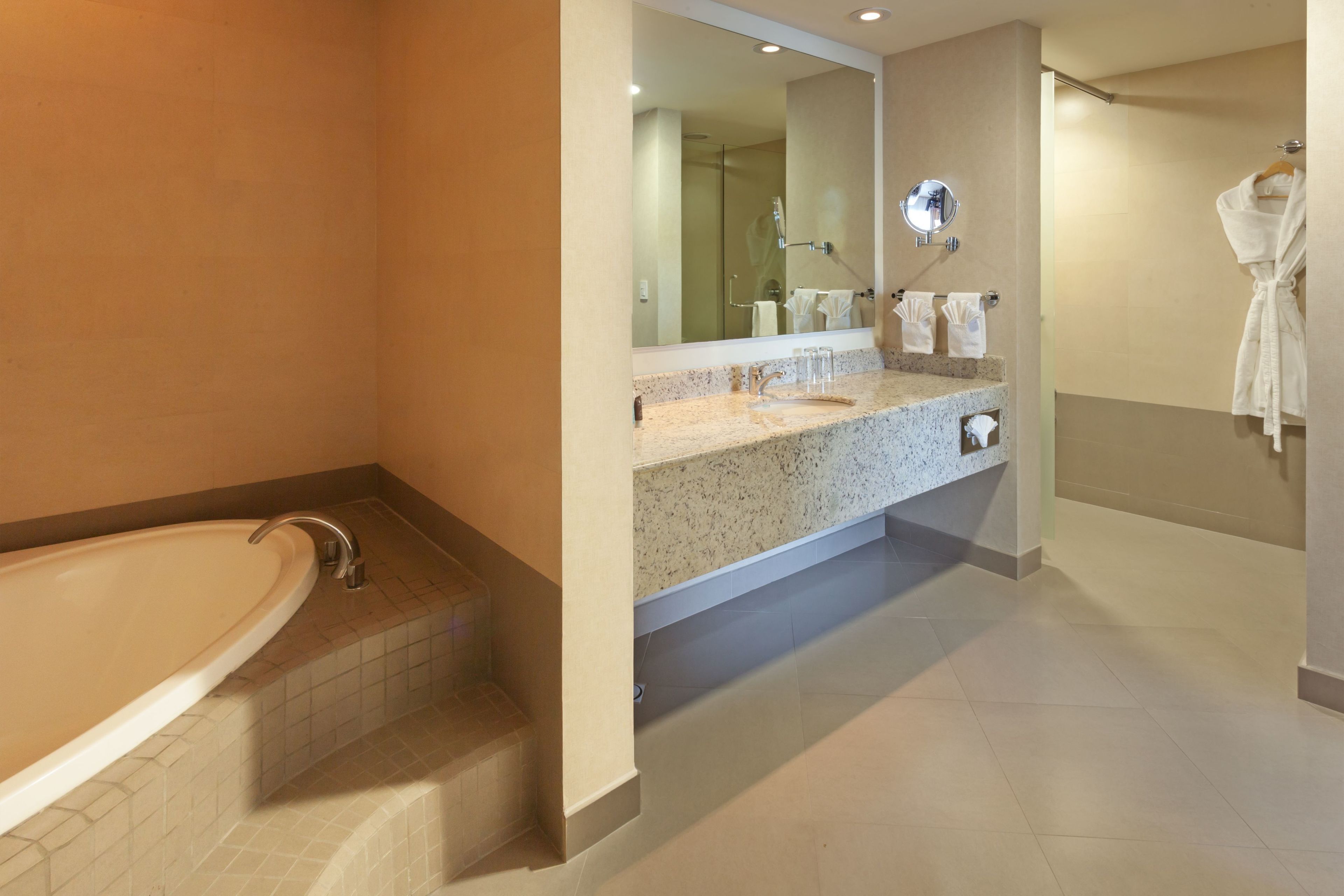 A modern bathroom with a freestanding bathtub, a granite countertop sink, a large mirror, and a robe hanging on the wall.