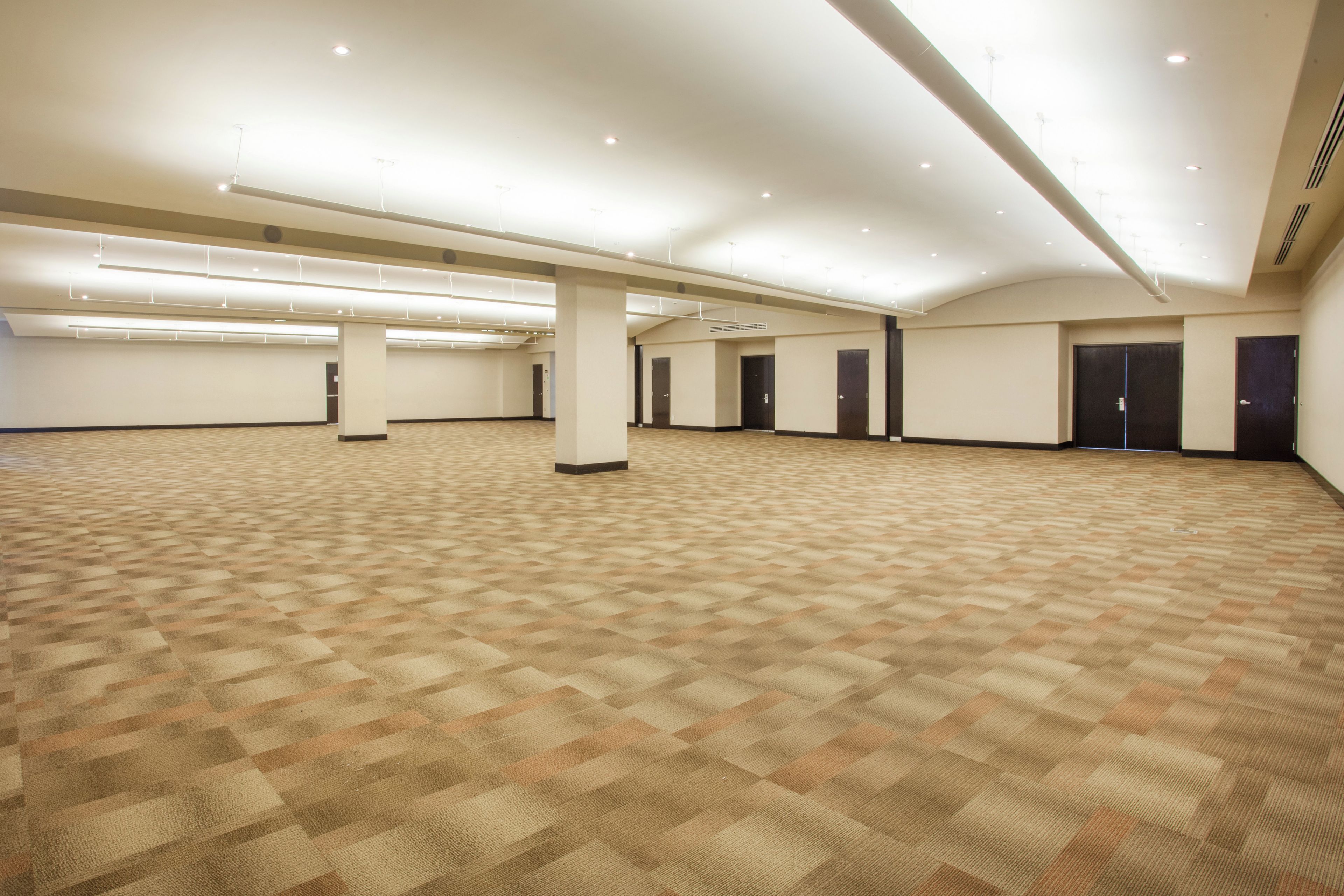A spacious indoor area with a patterned carpet, multiple doorways, and a high ceiling with recessed lighting.