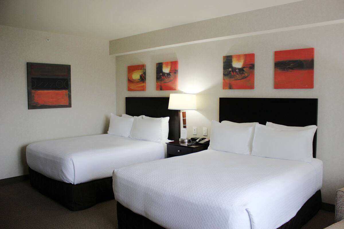 A hotel room with two single beds, a nightstand with a lamp, and three abstract paintings on the wall.