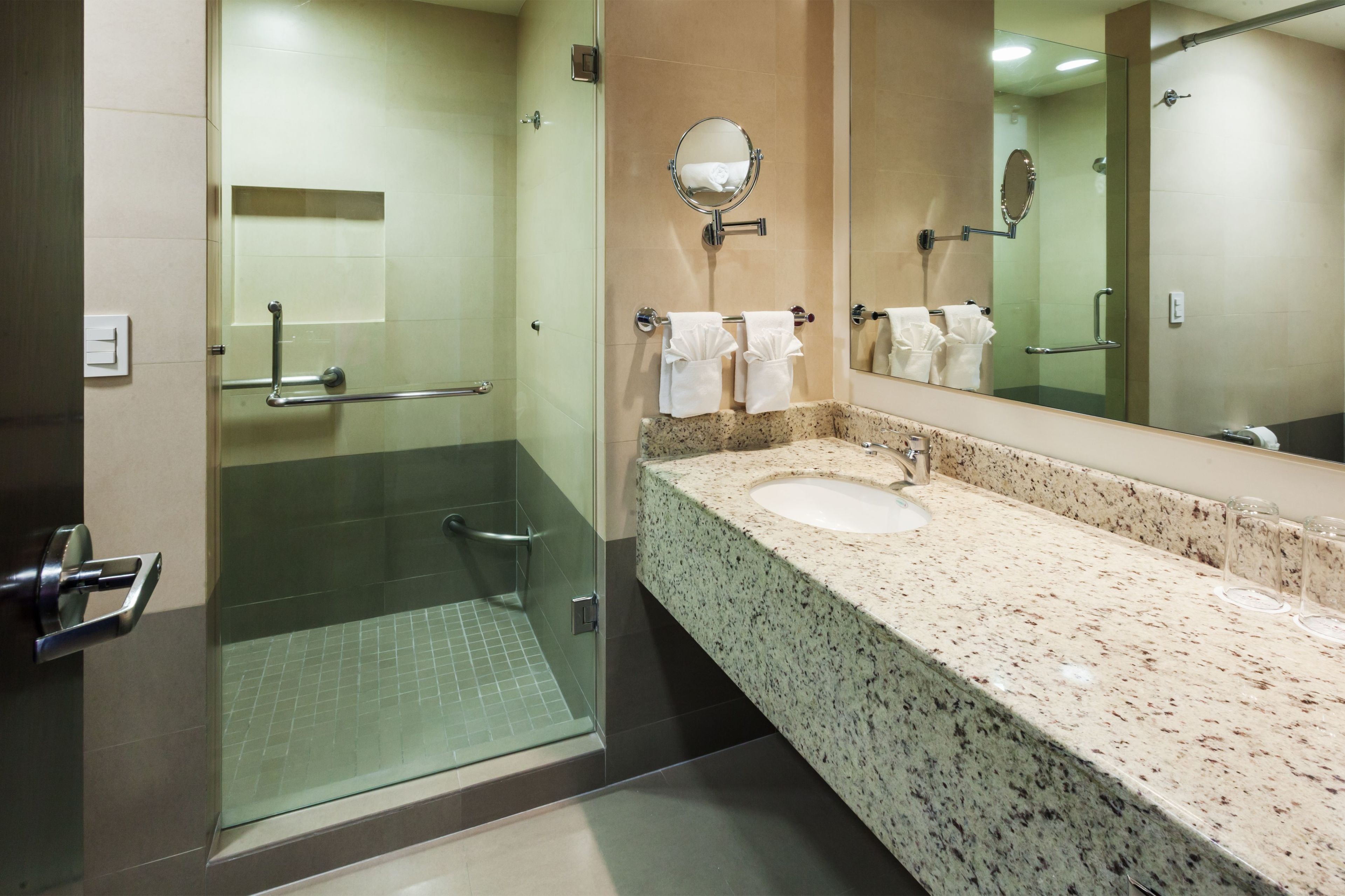 Un bagno moderno con box doccia in vetro, lavabo con piano in granito e uno specchio grande.