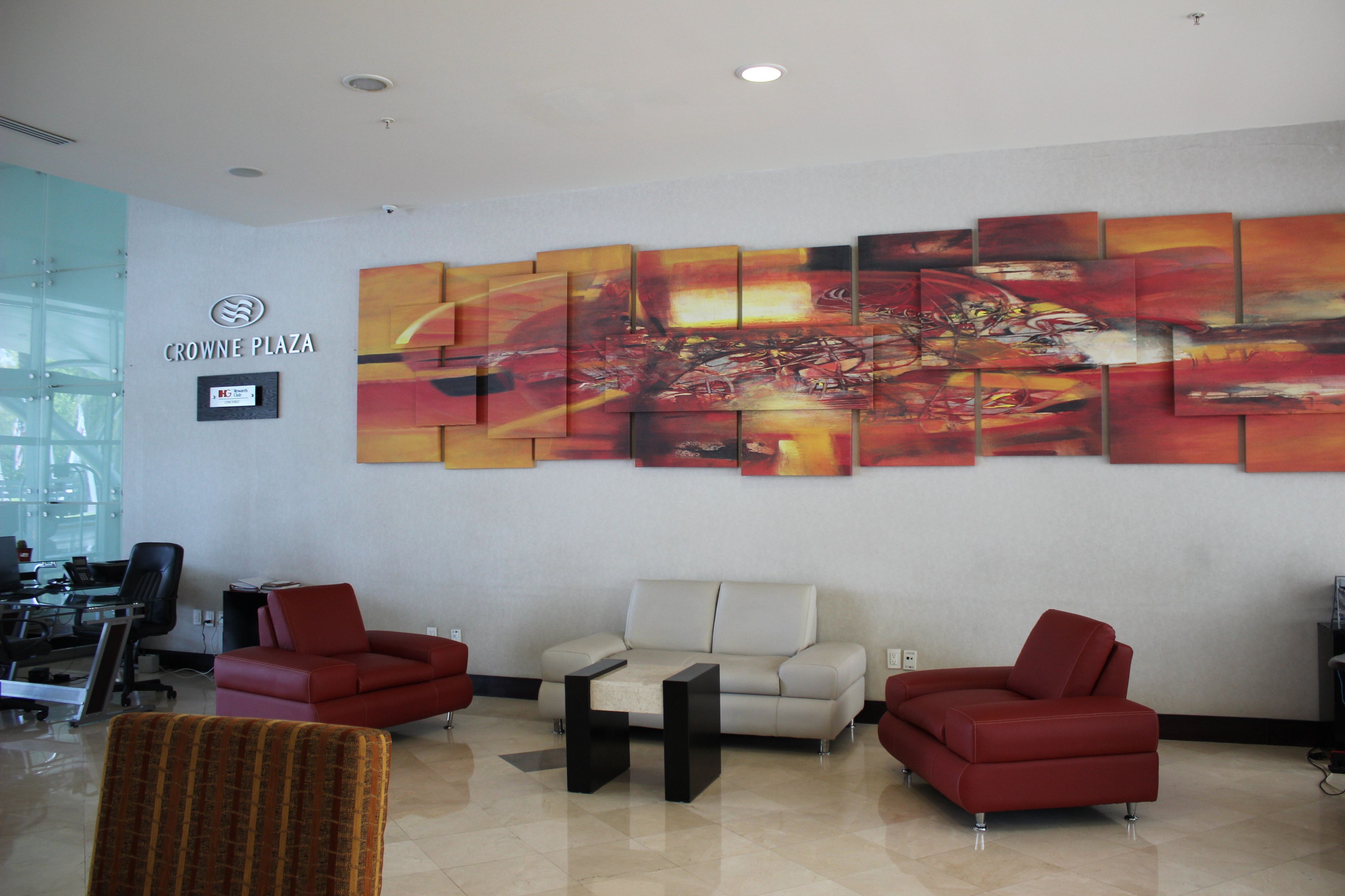 A lobby with a large abstract painting, a seating area with red chairs, a white sofa, and a glass partition.
