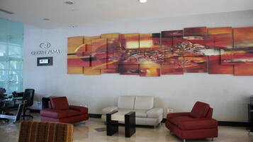 A lobby with a large abstract painting, a seating area with red chairs, a white sofa, and a glass partition.