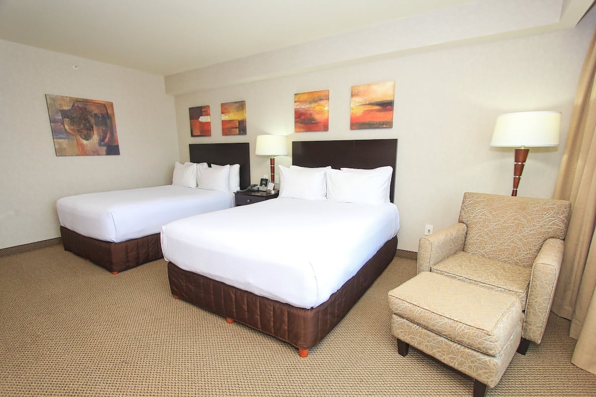 A hotel room with two beds, a chair, and artwork on the walls.