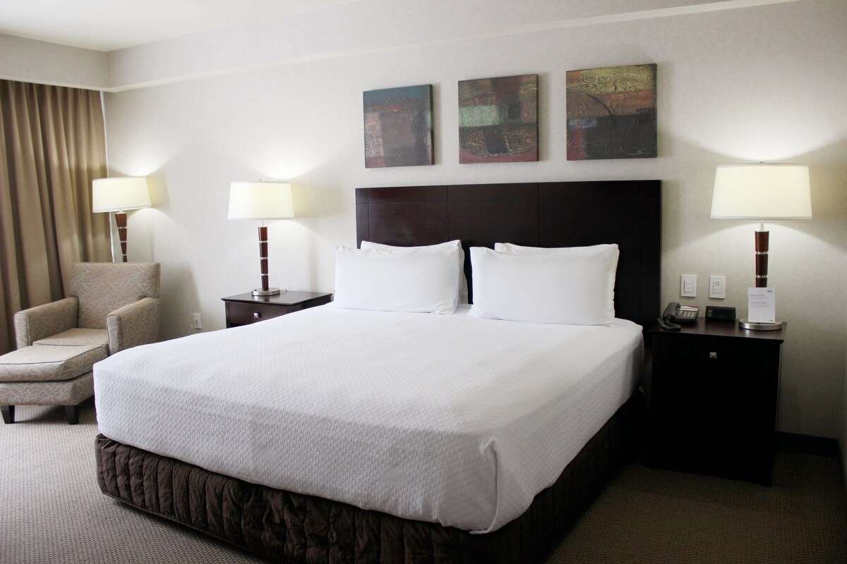 A hotel room with a large bed, two bedside tables with lamps, a chair, and artwork on the wall.
