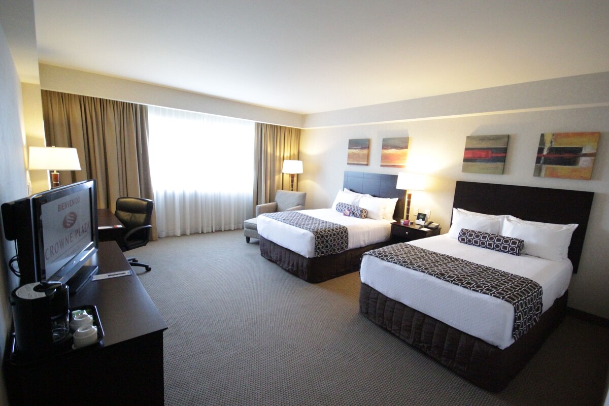 A hotel room with two beds, a desk with a television, and a chair.