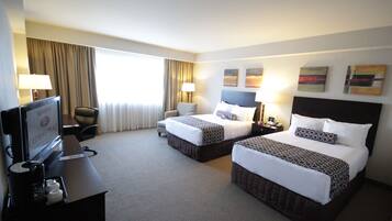 A hotel room with two beds, a desk with a television, and a chair.