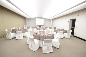 A conference room with round tables, white chairs, and a projector screen. - Crowne Plaza Leon by IHG (León)