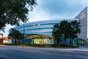 A modern building with a curved facade, a prominent entrance with a glass canopy, and palm trees in the foreground. - Crowne Plaza Leon by IHG (León)