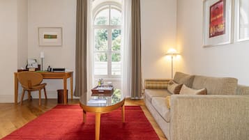 A living room with a red carpet, a wooden coffee table, a beige sofa, a desk with a chair, and a window with curtains.