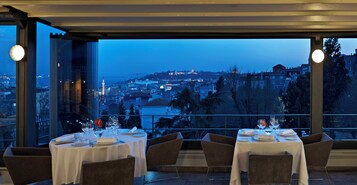 Ein Restaurant mit gedeckten Tischen, großen Fenstern mit Stadtblick und modernem Interieur.