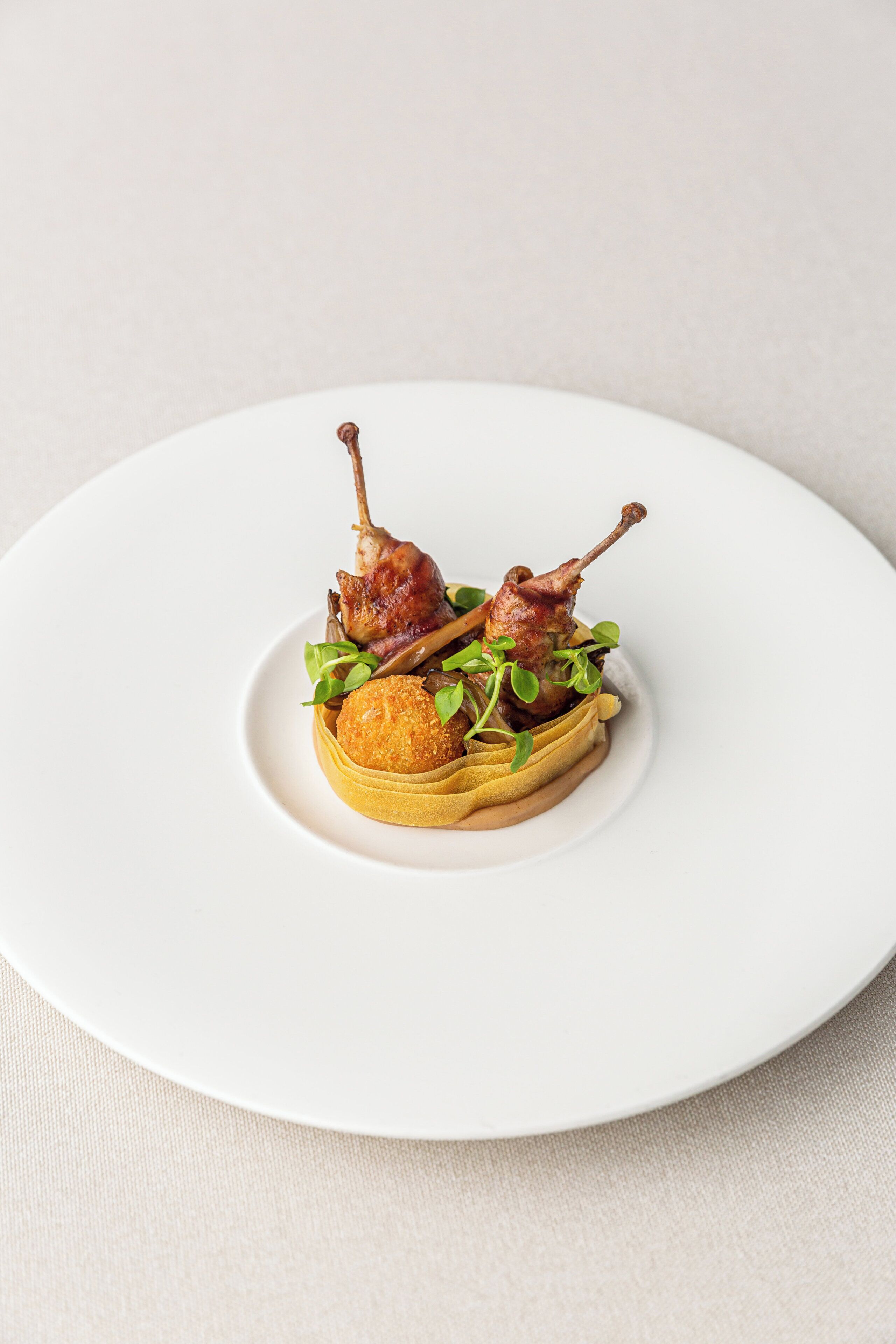 A white plate with two duck legs and a round item on a bed of greens.