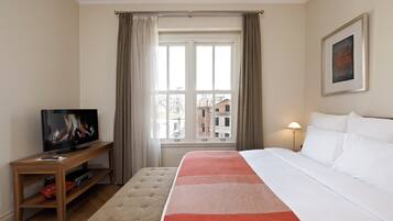 A hotel room with a bed, a TV on a wooden stand, a window with curtains, and a lamp.