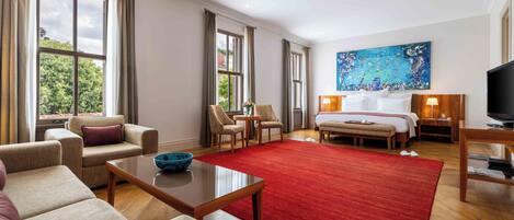 Habitación de hotel con un ventanal grande, alfombra roja, cama, televisión y un cuadro en la pared.