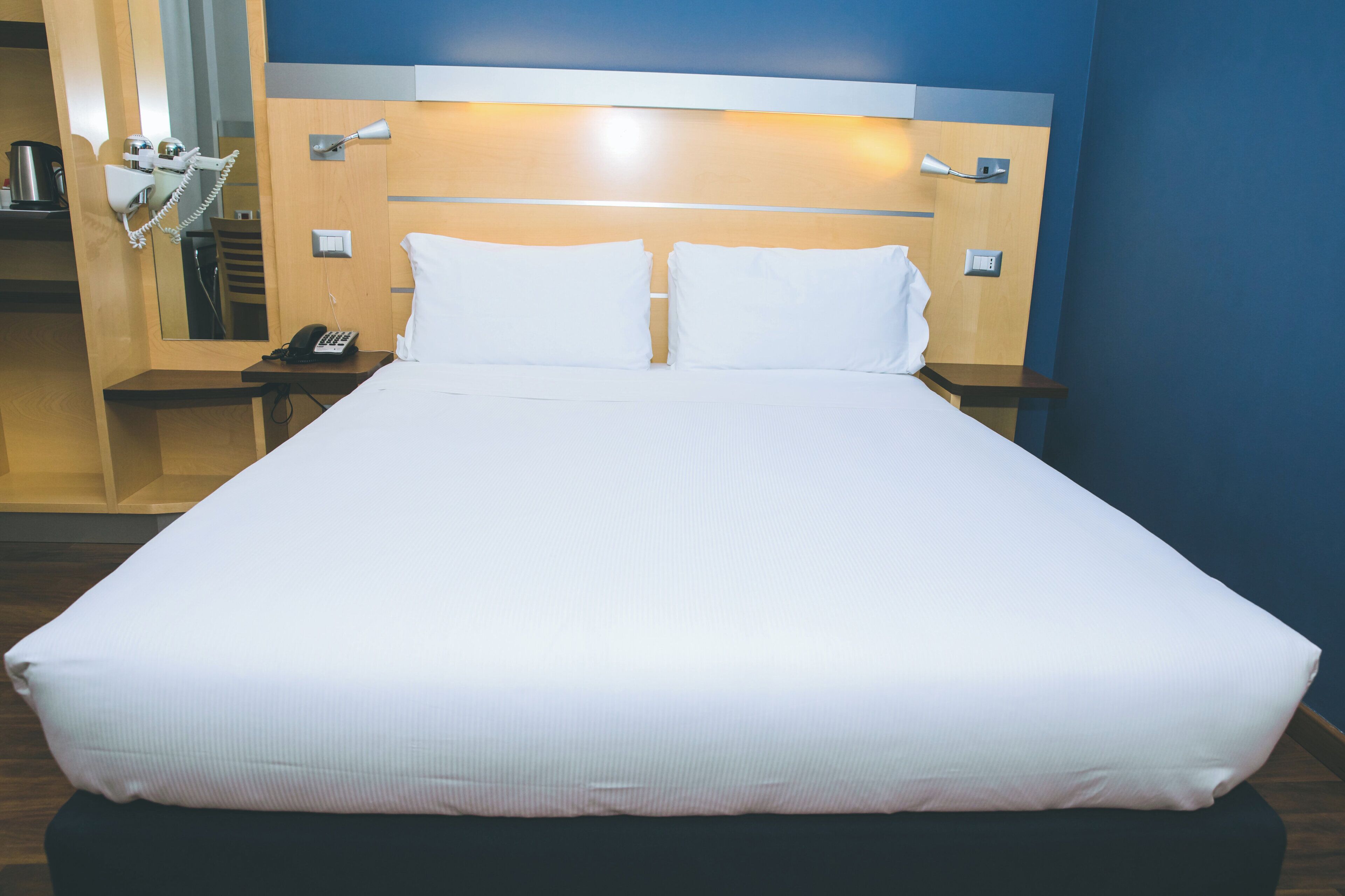 Une chambre d’hôtel avec un grand lit, deux tables de chevet, une commode, un téléphone et un miroir.