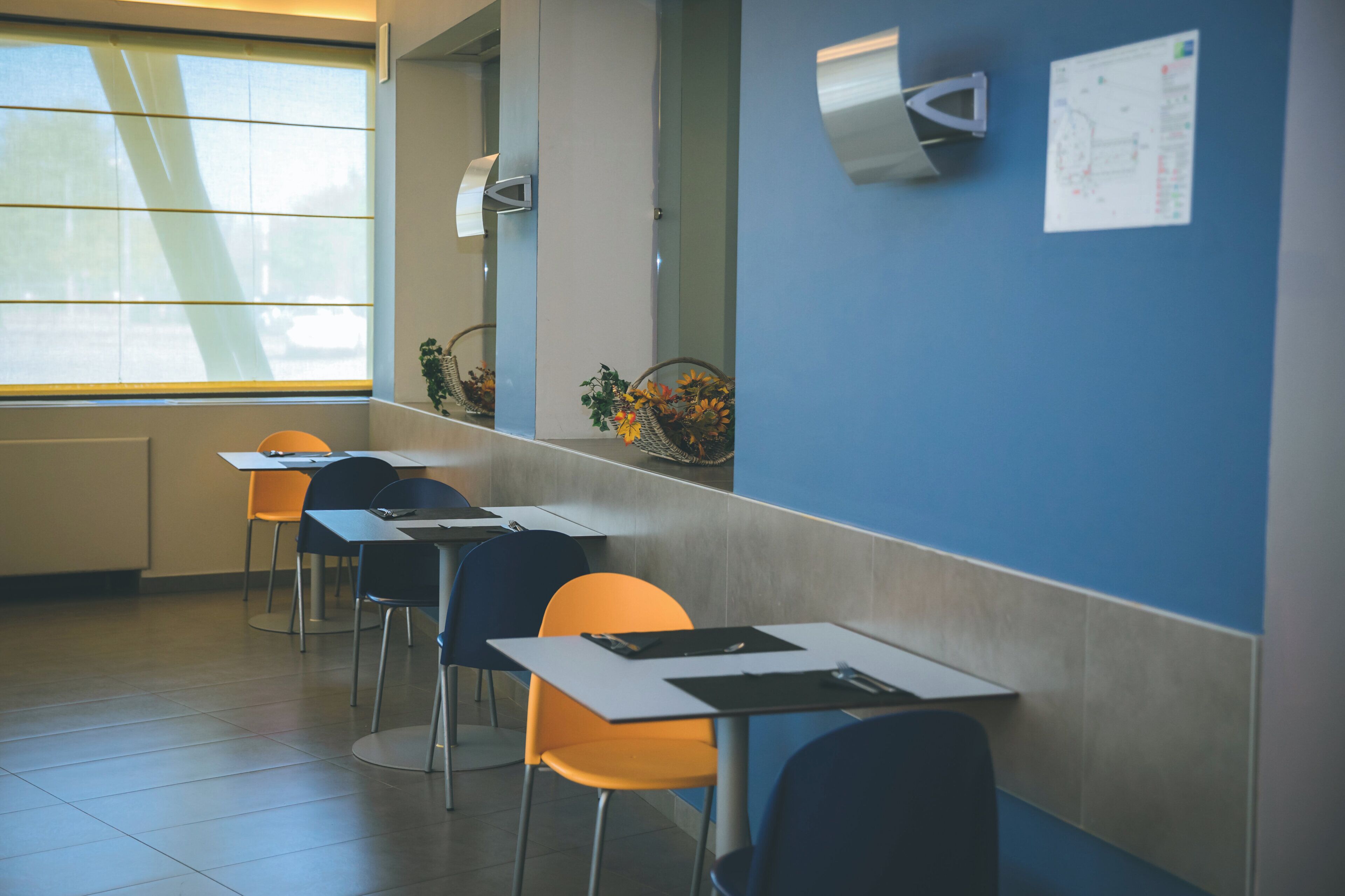 Uma sala de aula com mesas, cadeiras, uma janela e um aparelho de ar condicionado fixado na parede.