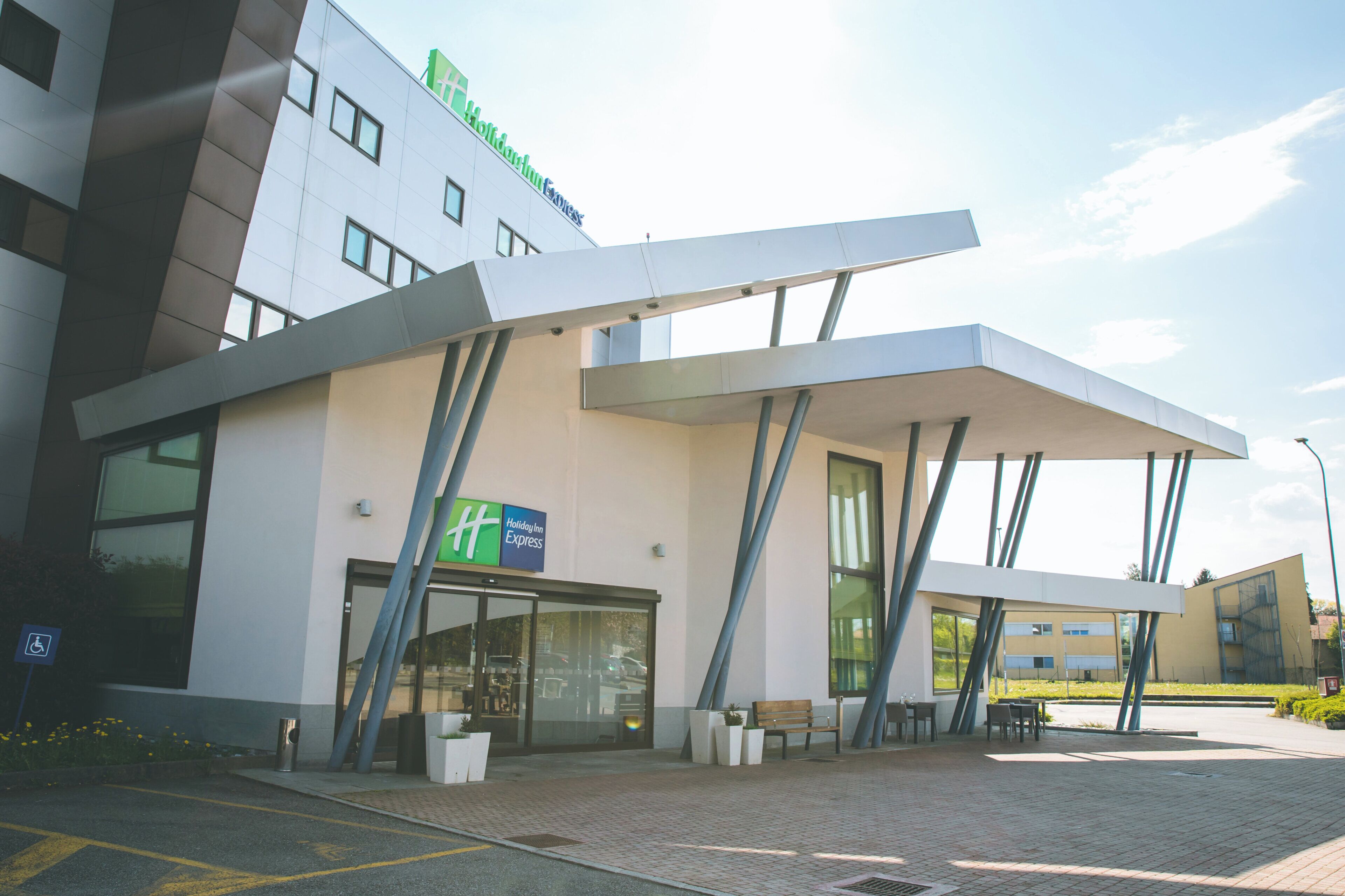 En modern byggnad med en skylt för Holiday Inn Express, stora fönster och ett takförsett utomhusområde med sittplatser.