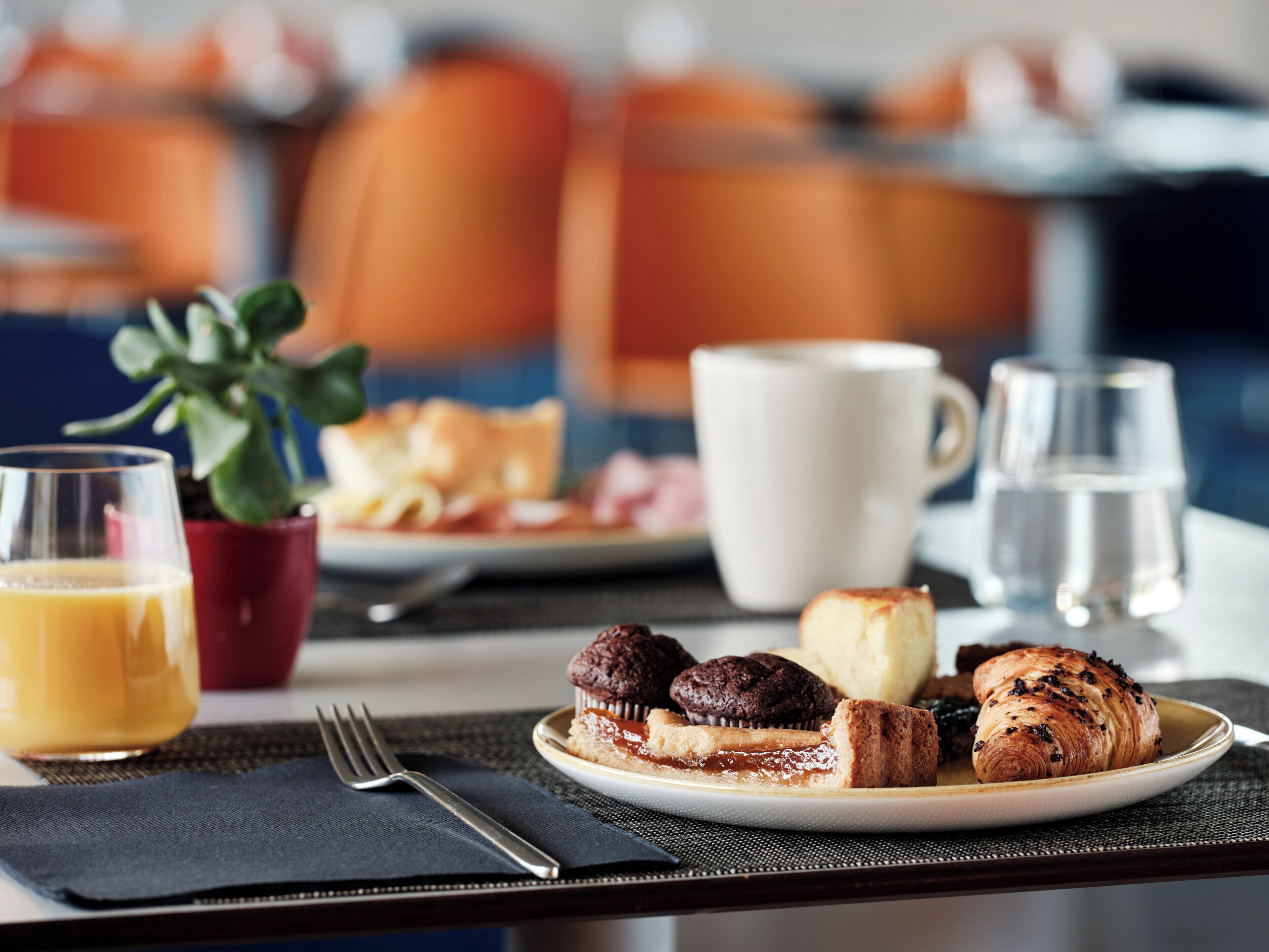 A breakfast setting with a plate of pastries, a cup of coffee, a glass of orange juice, and a small plant.
