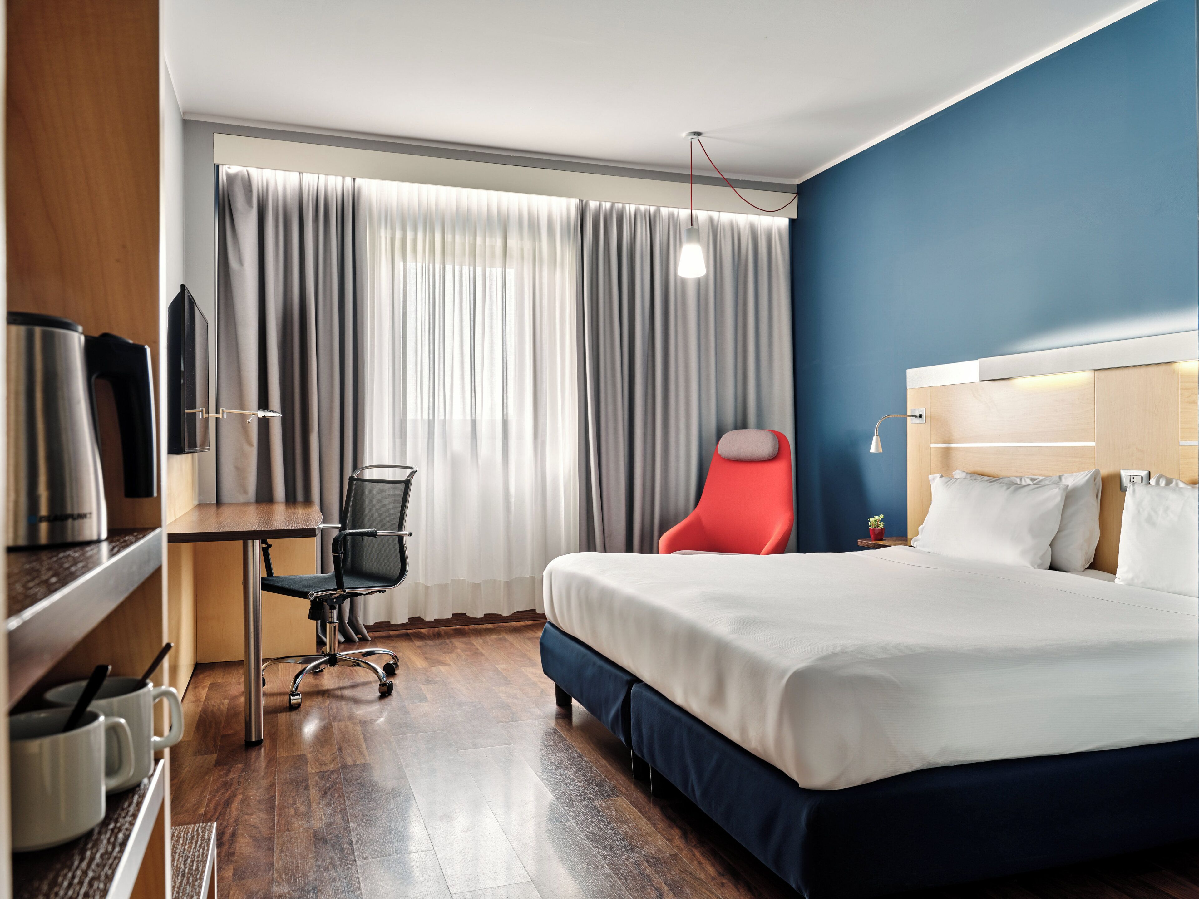 A hotel room with a bed, a desk, a chair, a television, and a window with curtains.