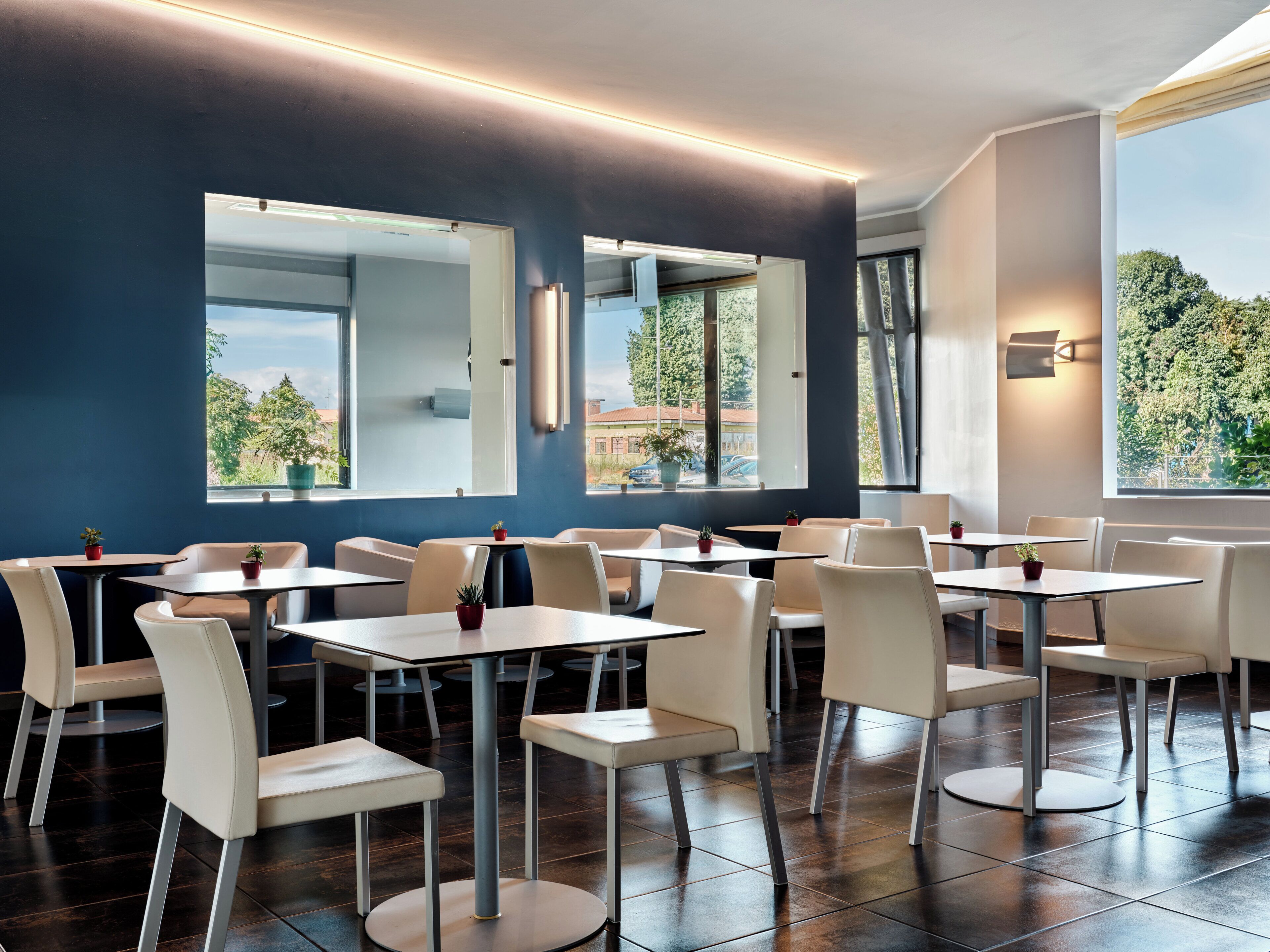 Un moderno comedor con mesas y sillas, ventanas amplias y vista a zonas verdes exteriores.