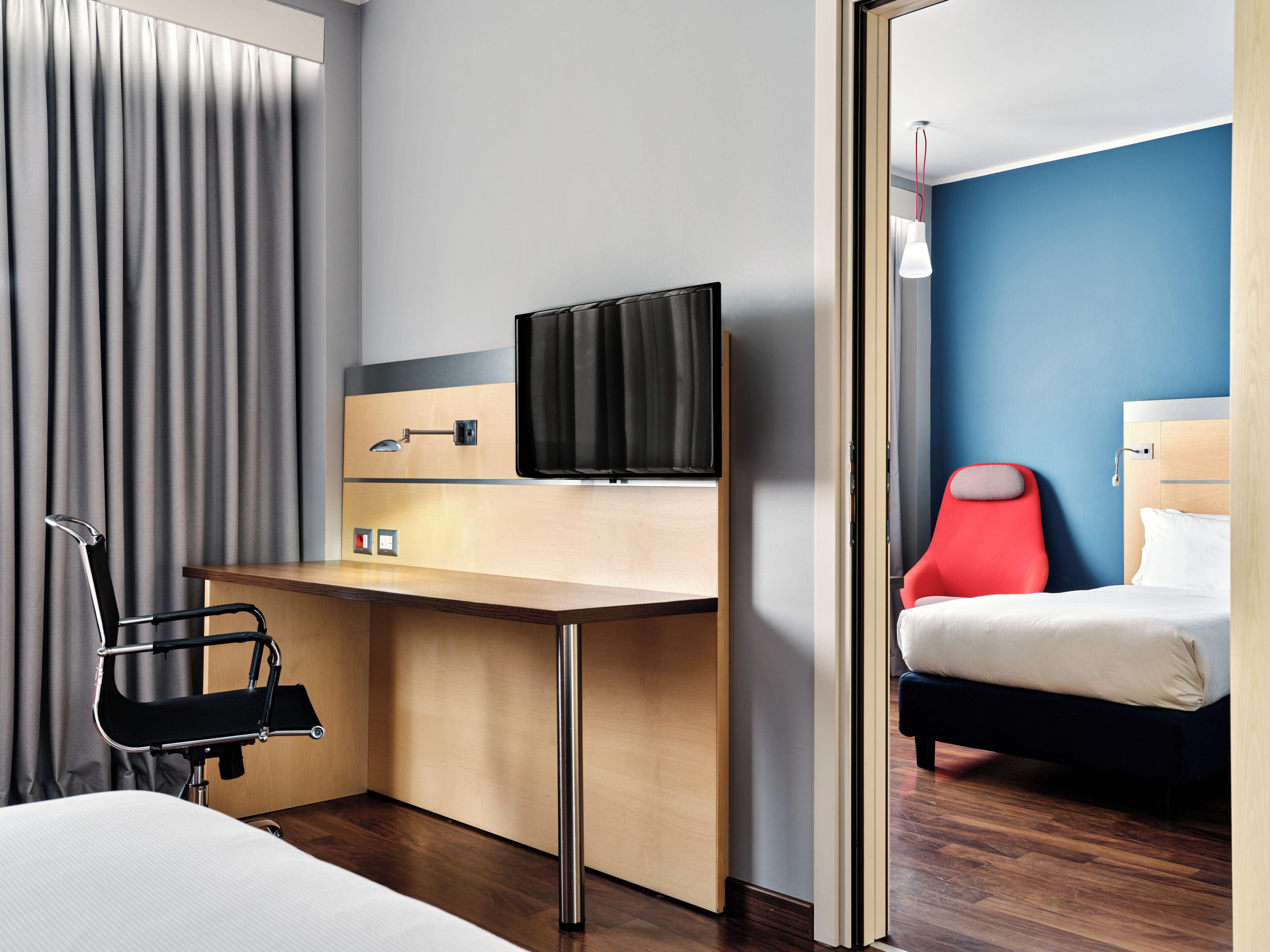 Ein Hotelzimmer mit Bett, Schreibtisch, Stuhl, Fernseher und Spiegel.