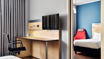 Habitación de hotel con cama, escritorio, silla, televisor y espejo.