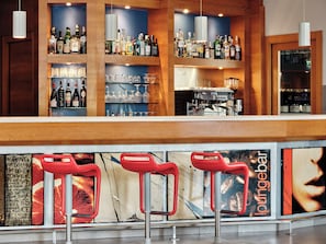 Zona de bar con estantes llenos de botellas de licor, vasos y una máquina de café.