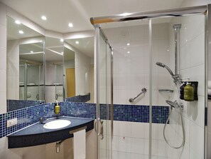 Un baño moderno con ducha de vidrio, lavamanos con salpicadero de azulejos azules y espejo sobre el lavamanos.