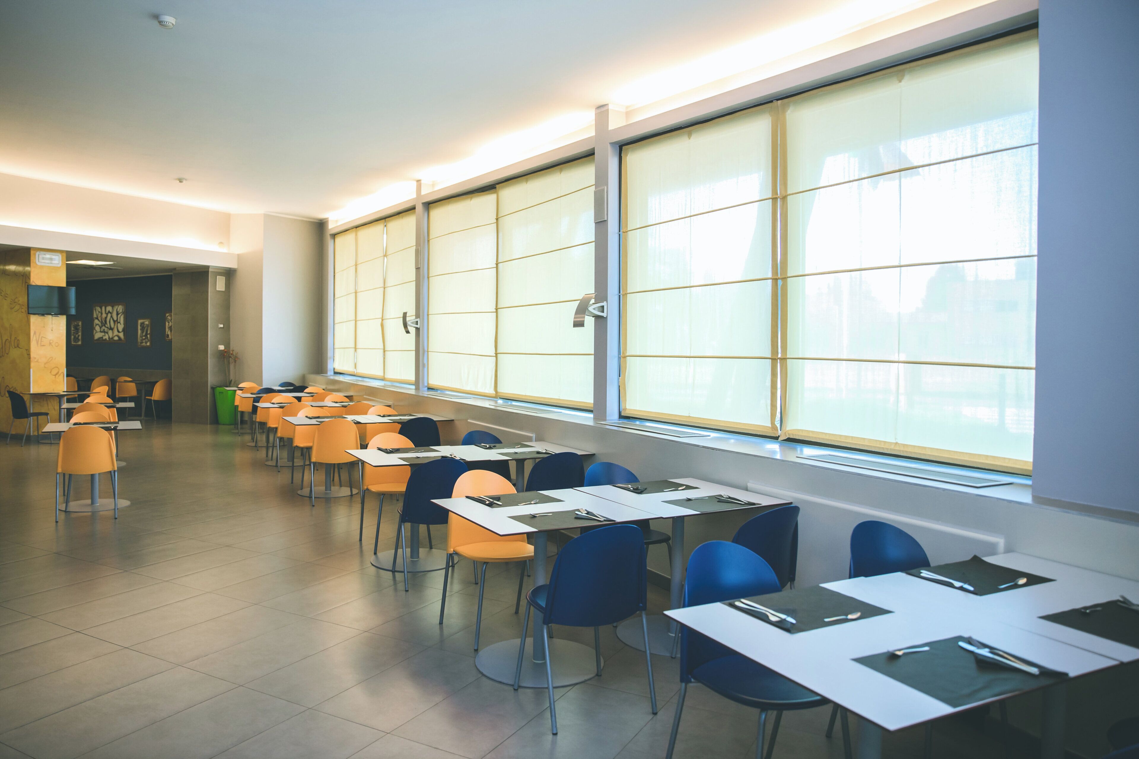 Un aula con filas de escritorios y sillas, ventanas amplias y piso de baldosas.