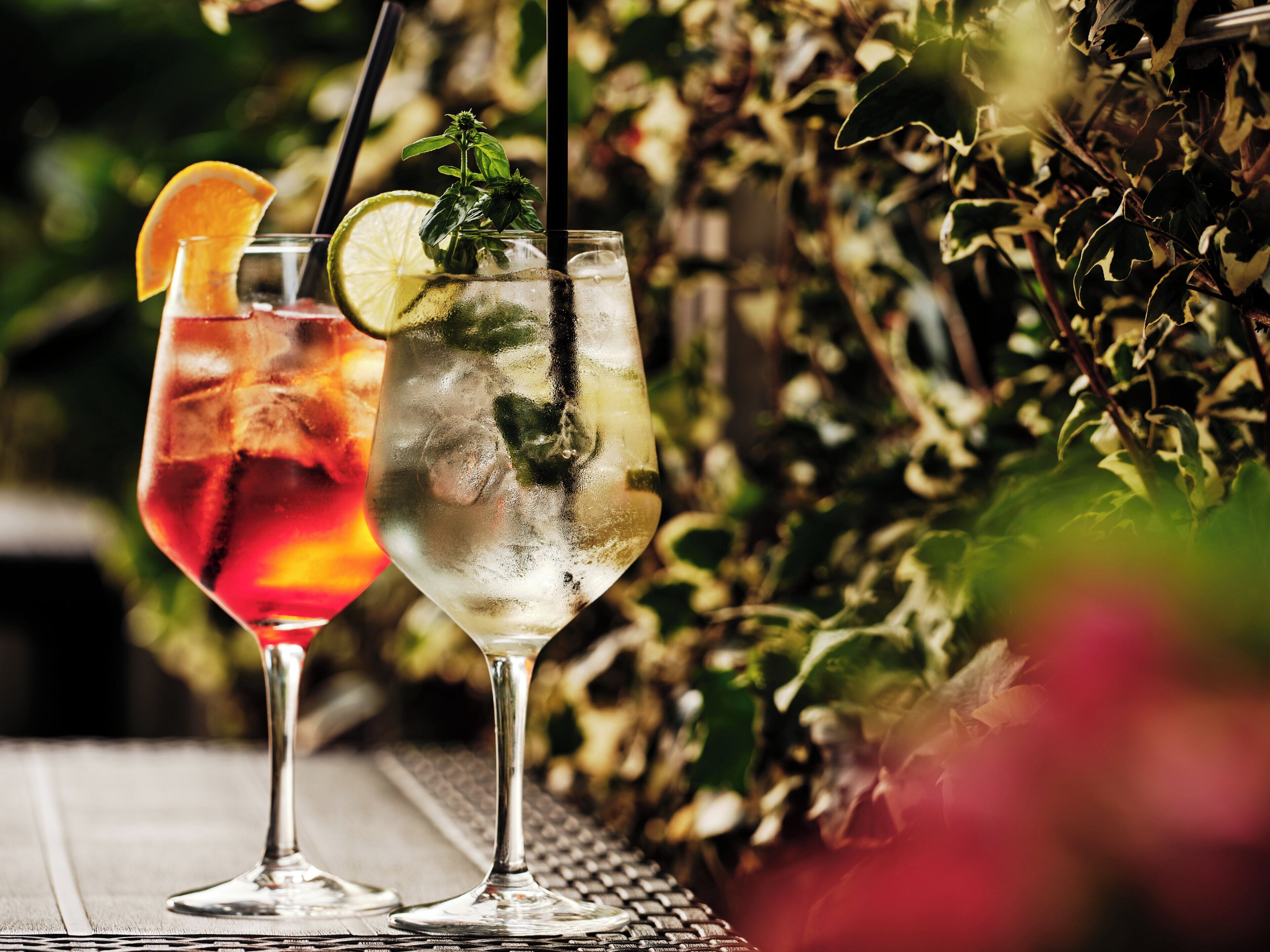 Deux verres de boissons glacées, décorées de fruits ou d’autres éléments, sont posés sur une table à l’extérieur.