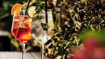 Deux verres de boissons glacées, décorées de fruits ou d’autres éléments, sont posés sur une table à l’extérieur.