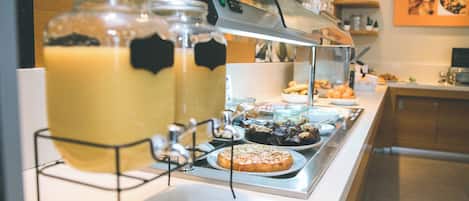 A buffet setup with a coffee station, various pastries, and a selection of fruits.