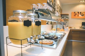 Montaje de bufé con estación de café, diversas opciones de pastelería y una selección de frutas.