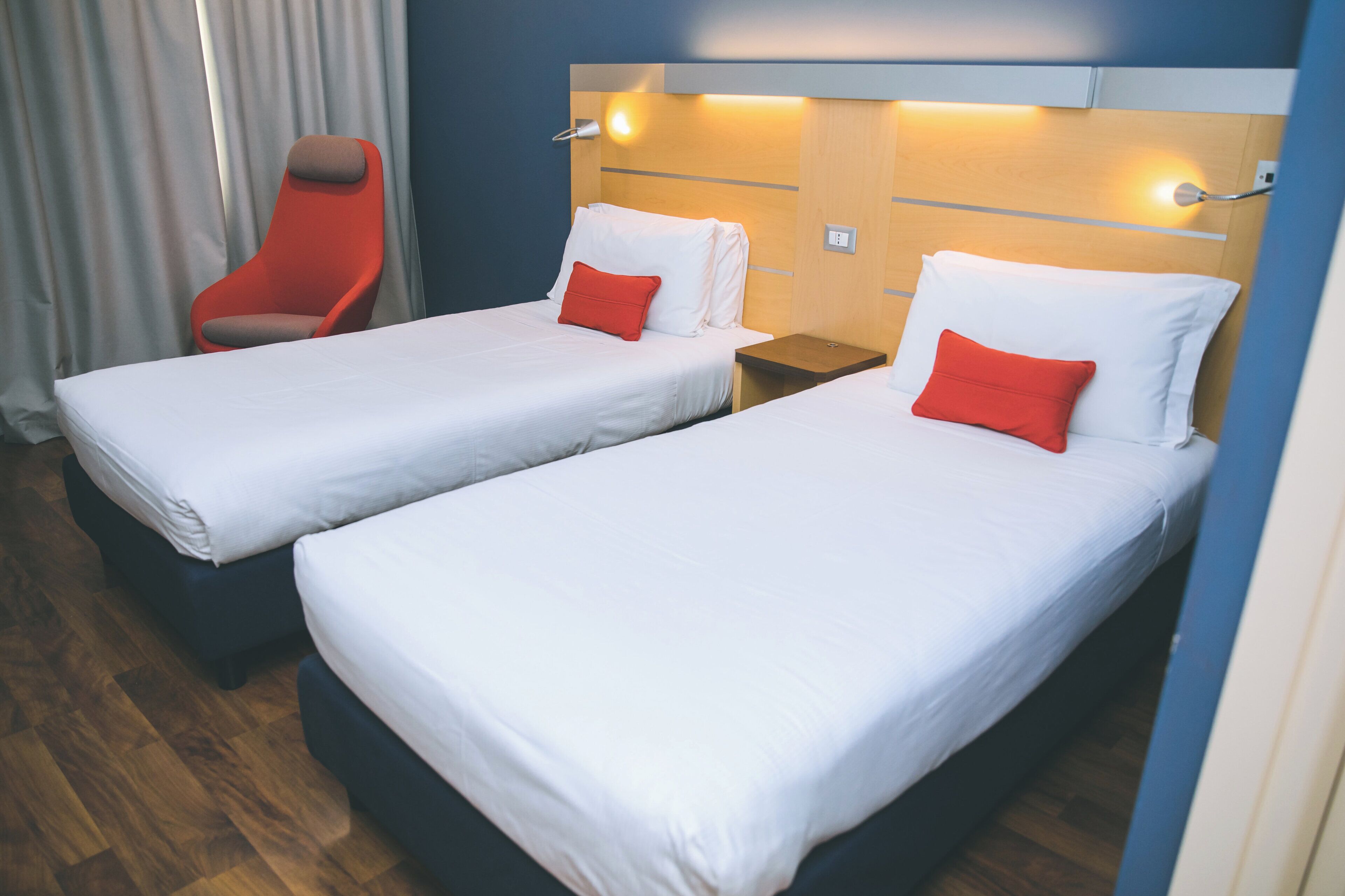 A hotel room with two single beds, a red chair, and a wooden headboard.