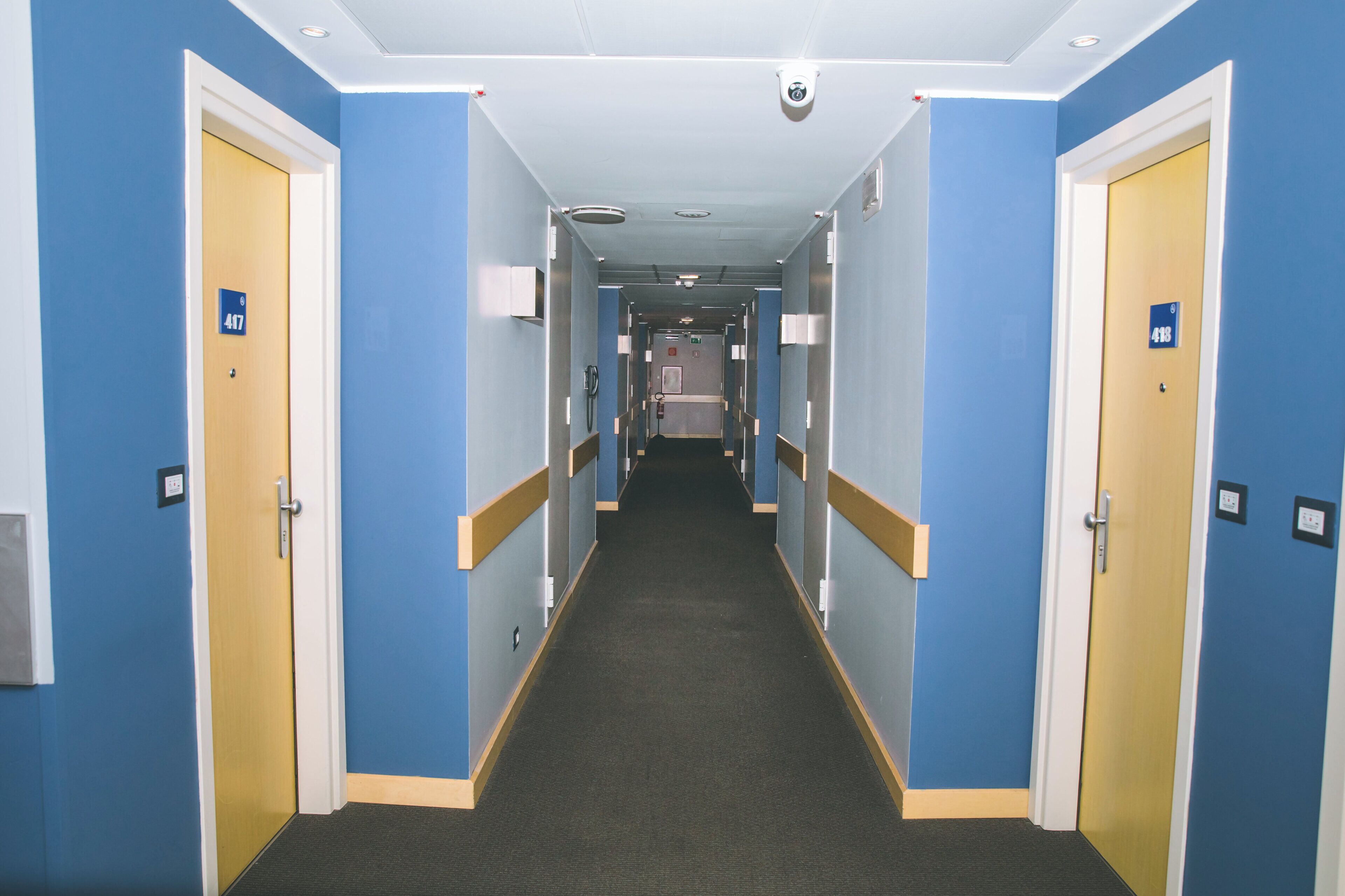 Un pasillo de hotel con paredes azules, puertas de madera y pisos alfombrados.