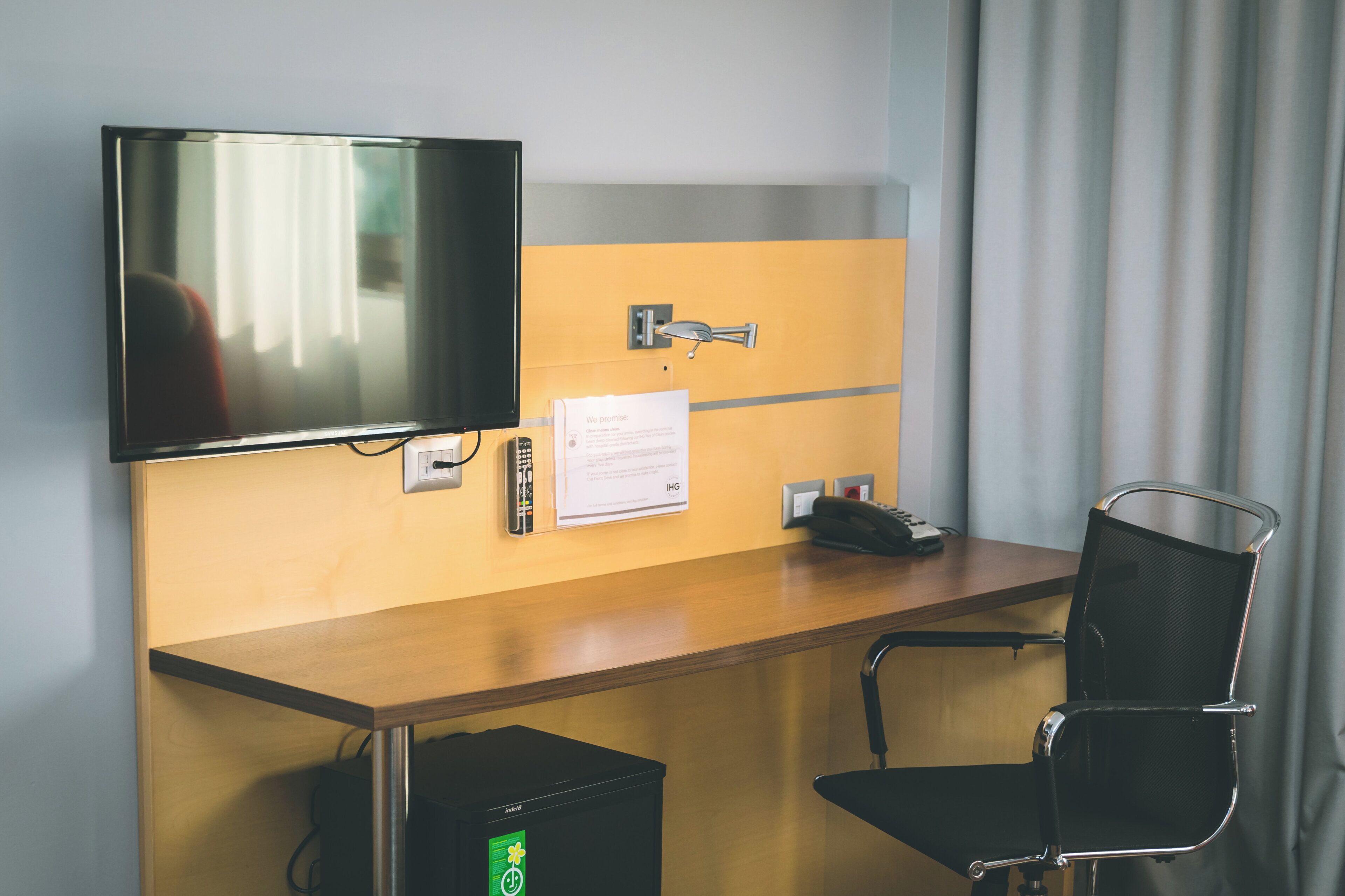Hotelkamer met een houten bureau, een zwarte bureaustoel, een flatscreen televisie aan de muur, een telefoon en een kleine prullenbak.