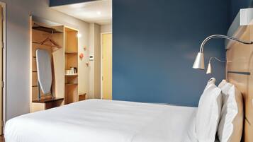 Une chambre d’hôtel avec un lit bien fait, une armoire, un vêtement suspendu et une lampe de chevet.