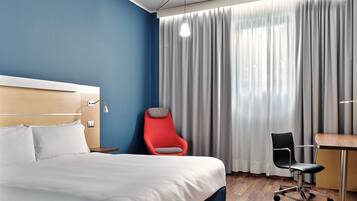 Ein Hotelzimmer mit Bett, Schreibtisch, Stuhl und einem Vorhangfenster.