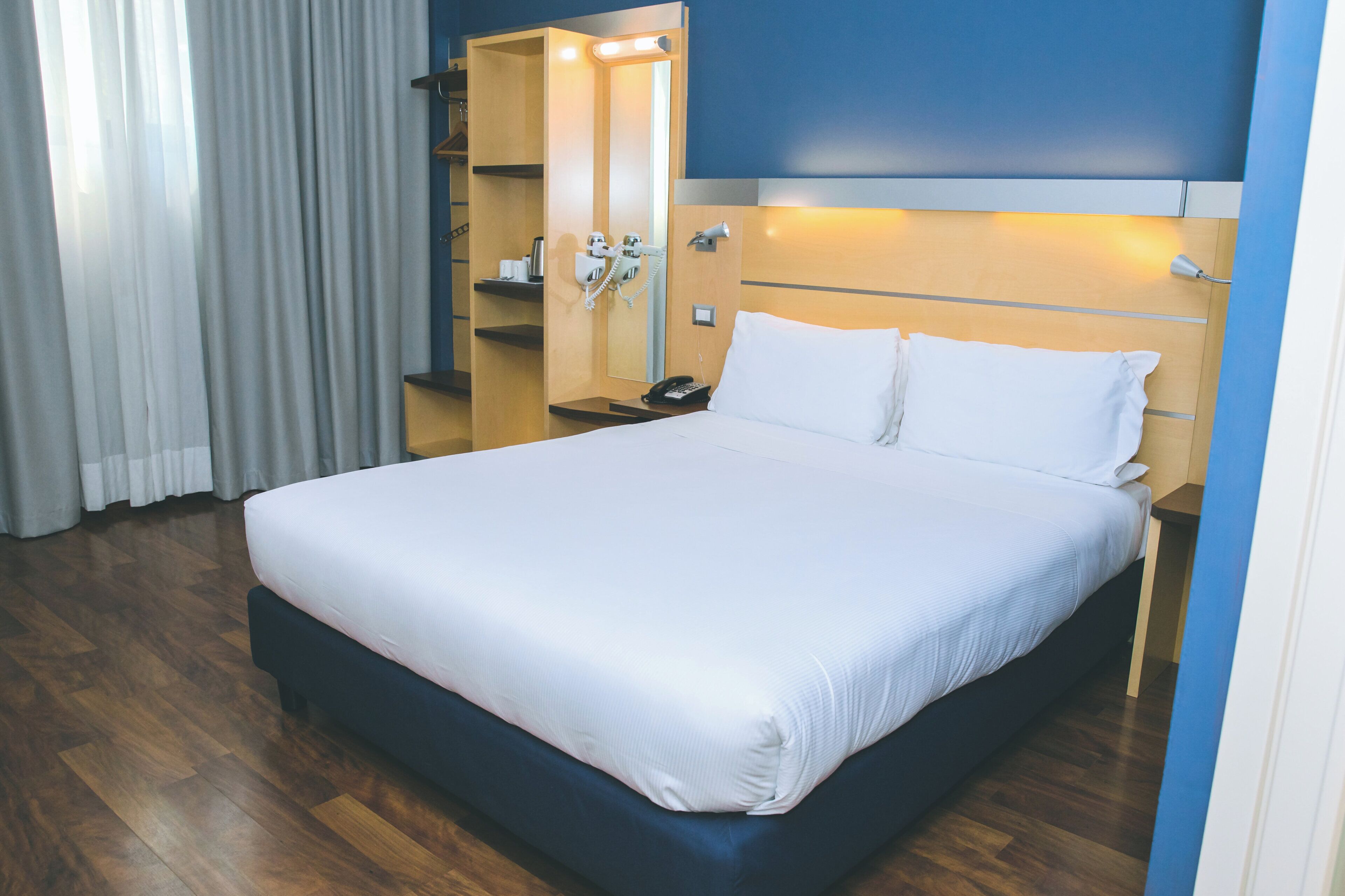 Una camera d'albergo con un letto grande, un comodino con il telefono e uno specchio.